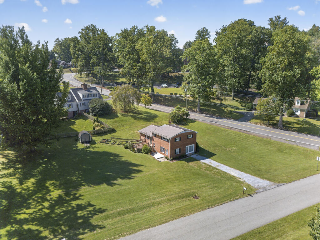 Aerial view of a two-story brick house and broad lawn beside a tree-lined road.