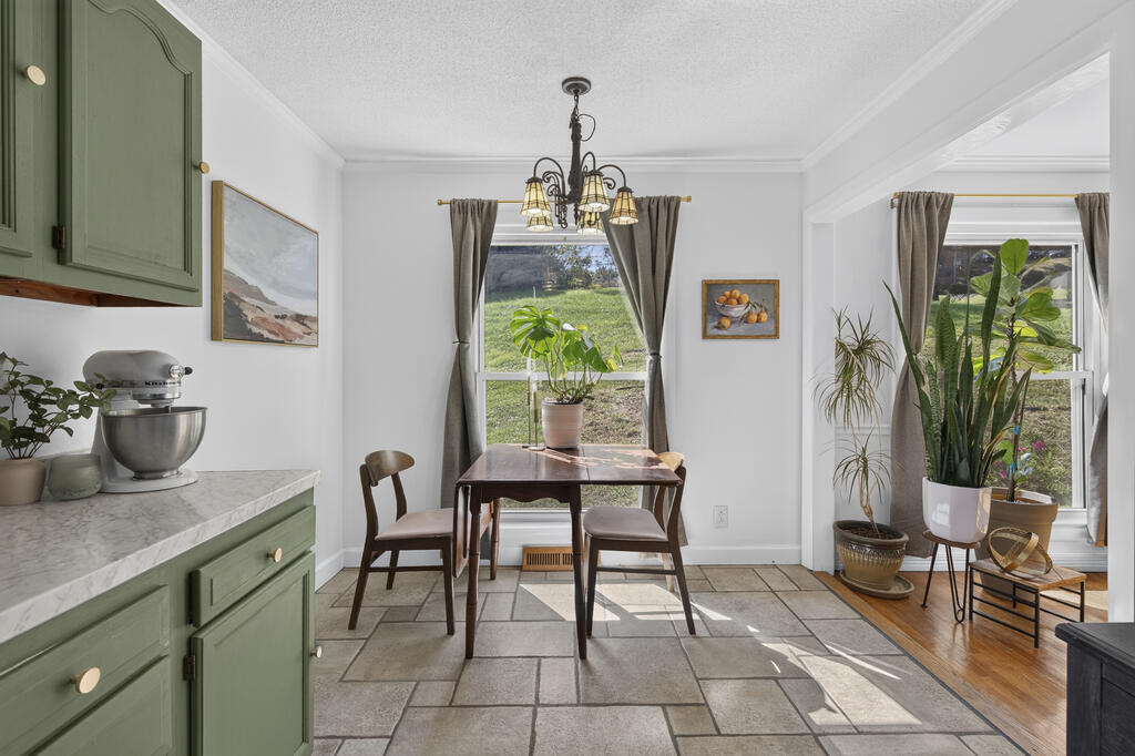 Kitchen dining area with sage-green cabinets, tiled floors, a wooden table, and large curtained windows.