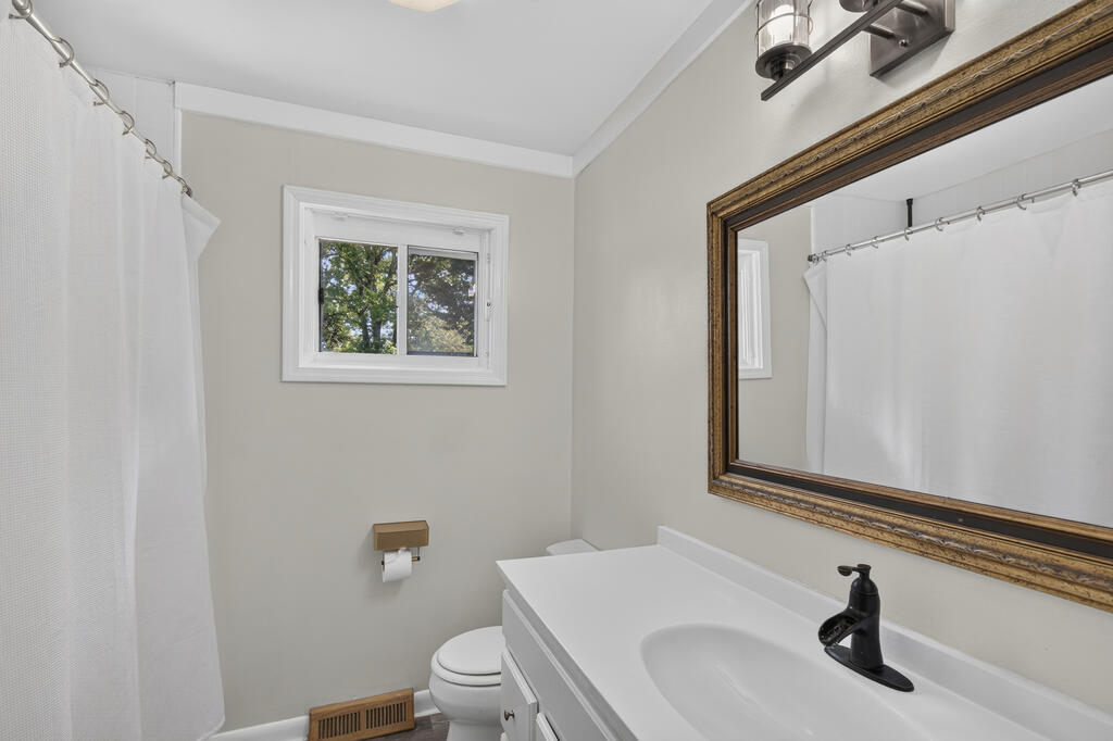 Bathroom with a white vanity, black faucet, large framed mirror, and curtained shower.