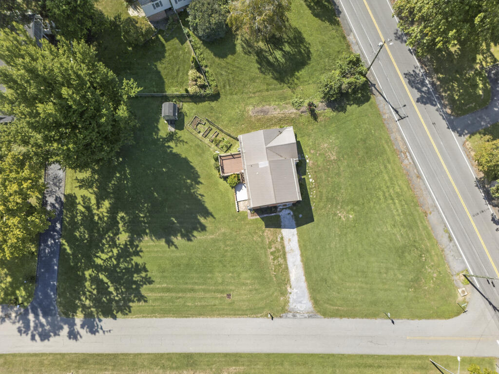 Aerial view of a house on a large grassy lot beside two roads, with mature trees.