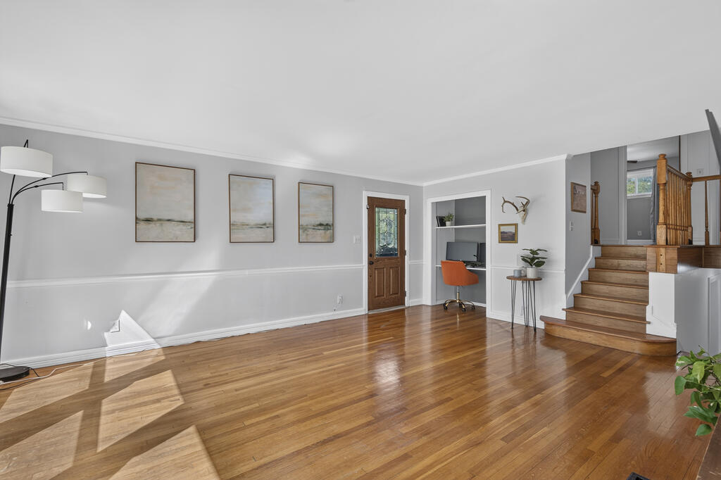 Living room with polished hardwood floors, a built-in desk nook, and stairs with wooden railings.