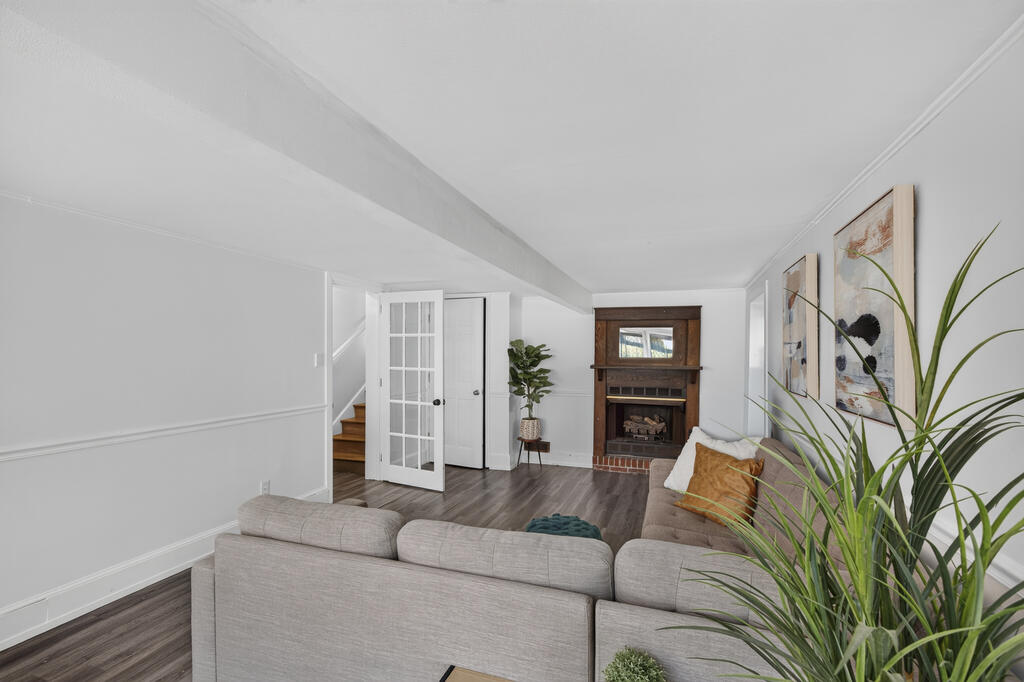 Living room with a gray sectional, brick fireplace, glass-paneled door, and staircase.
