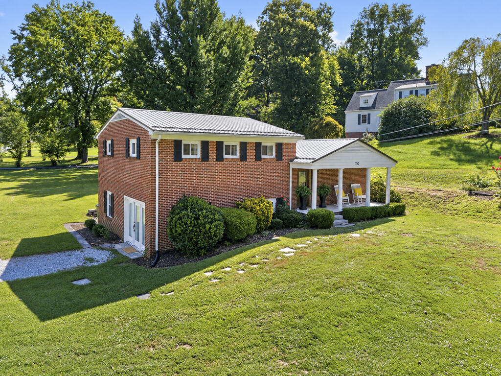 Two-story brick house with a metal roof and covered porch on a tree-lined lawn.