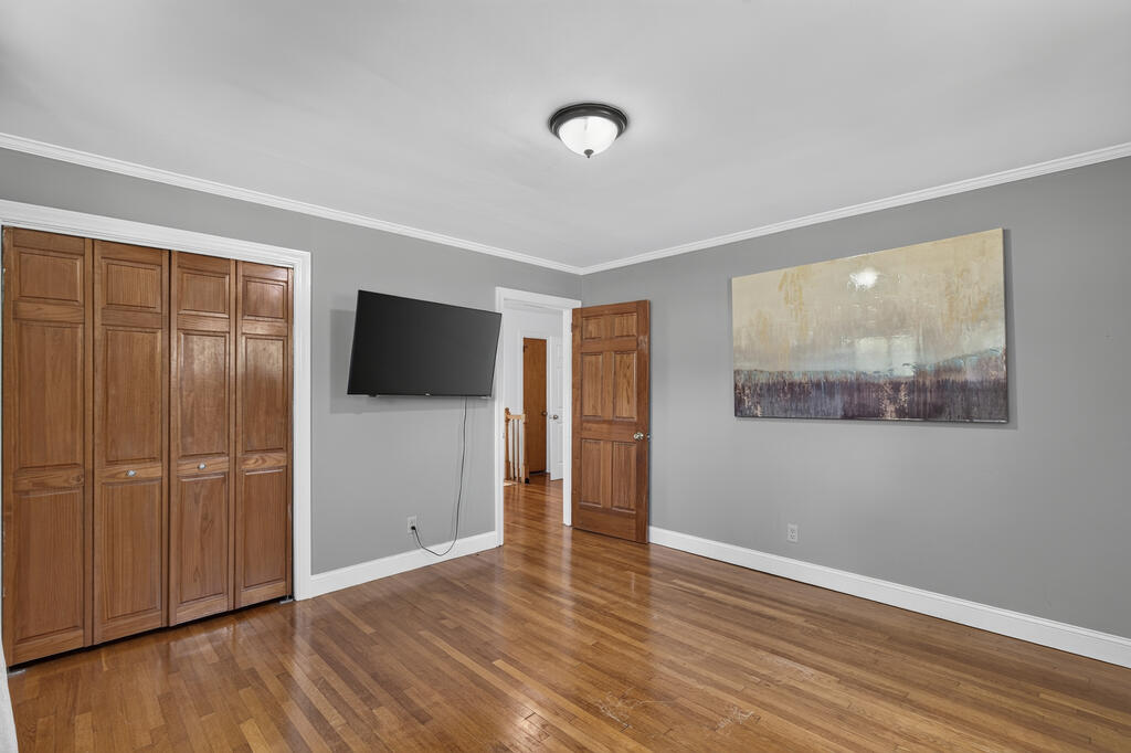 Room with built-in wooden closets, hardwood flooring, and a wall-mounted television.