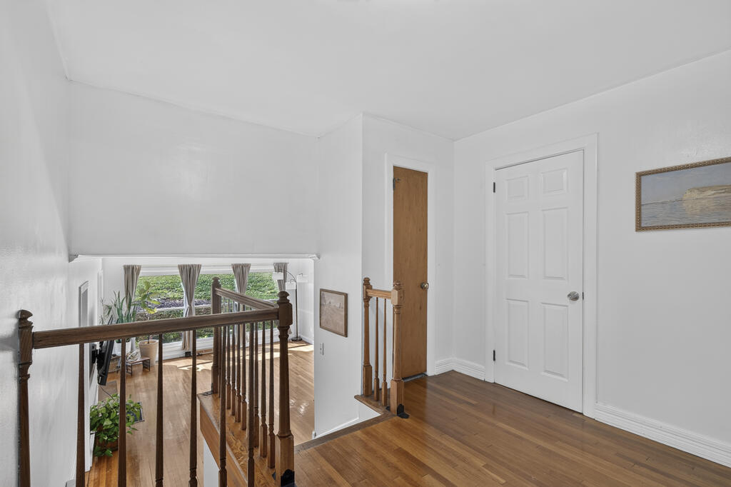 Upstairs landing with hardwood floors and dark wood railings overlooking a bright living area.