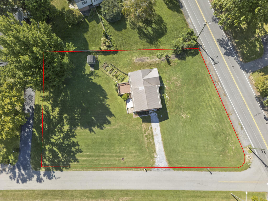 Aerial view of a house on a large red-outlined grassy lot beside two roads.