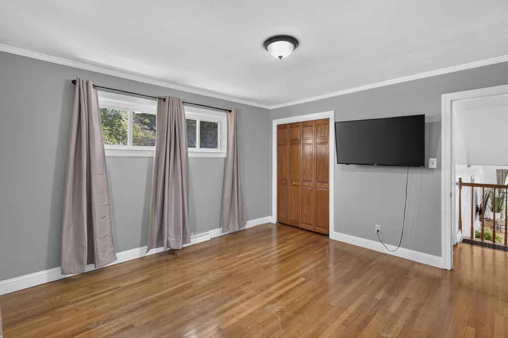 Empty room with hardwood floors, curtained windows, a wooden closet, and a wall-mounted television.