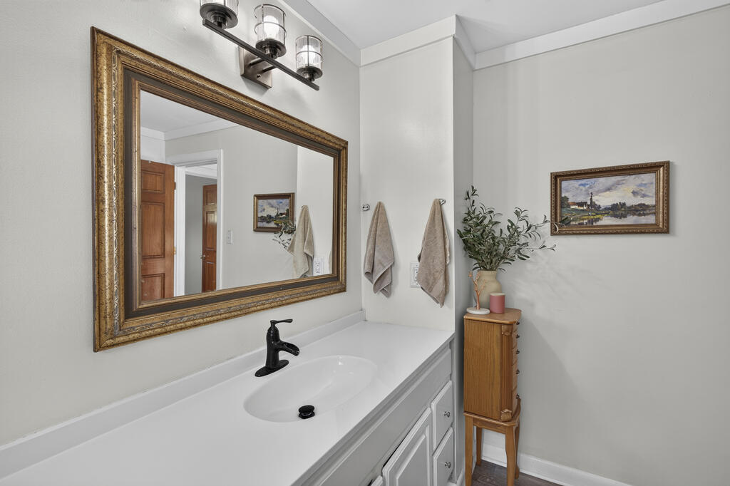 Bathroom vanity with a large ornate mirror, white countertop, and black faucet.