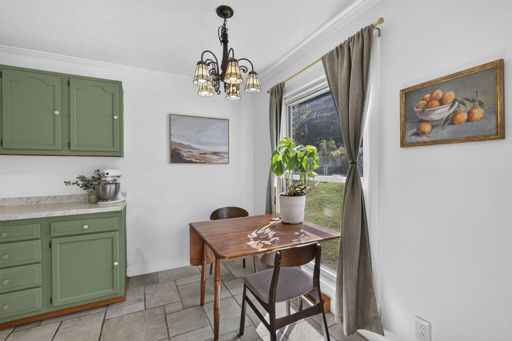 Kitchen dining nook with sage-green cabinets, a wooden table, and a large curtained window.