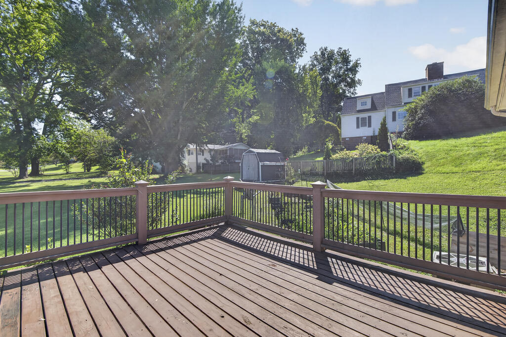Wooden deck overlooks a fenced, tree-shaded lawn with a small storage shed.