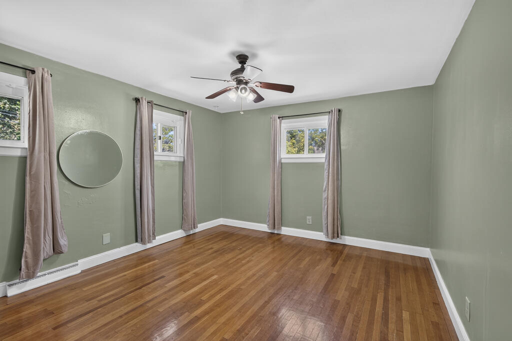 Empty bedroom with hardwood floors, sage-green walls, and three curtained windows.