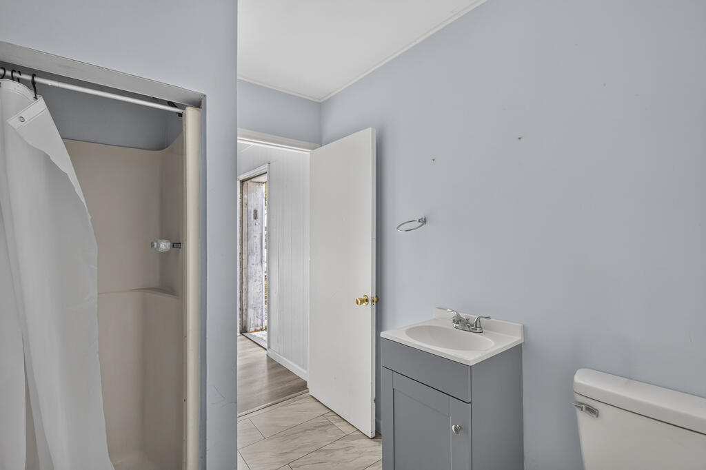 Bathroom with a shower, gray vanity, white sink, and open door to the hallway.