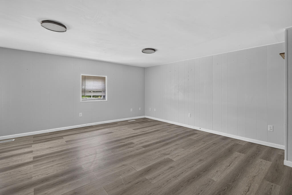 Empty room with gray paneled walls, a small window, and wood-look flooring.