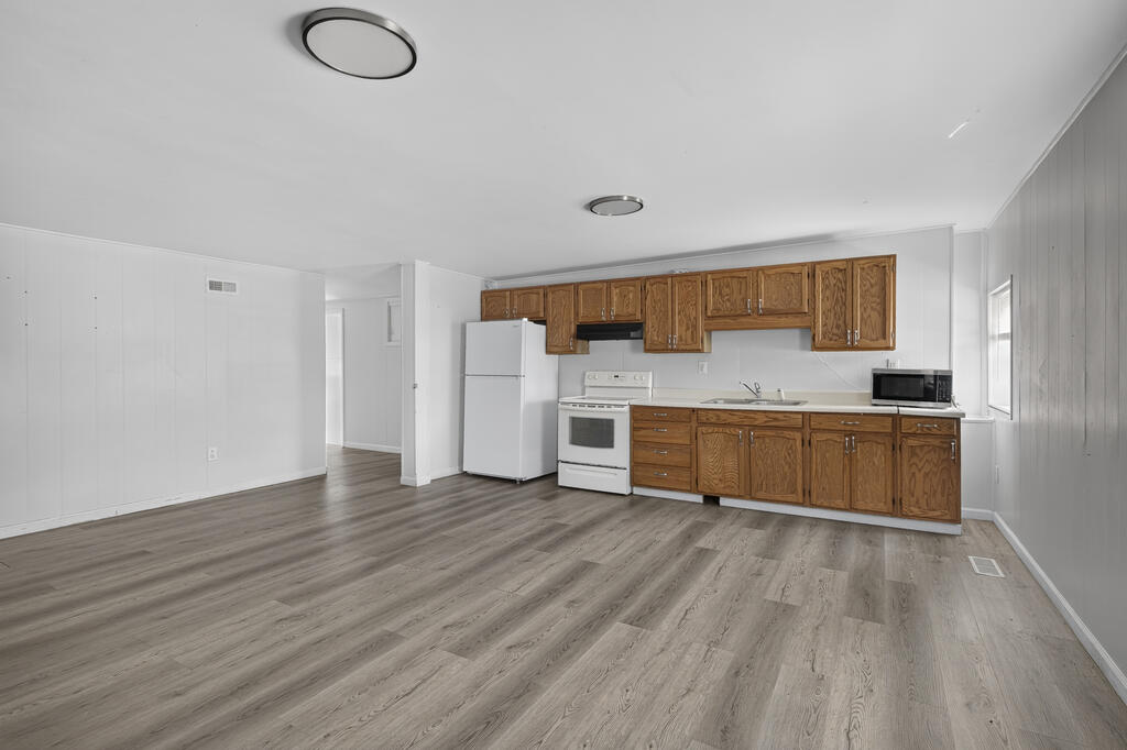 Empty kitchen with brown wood cabinets, white appliances, and gray plank flooring.