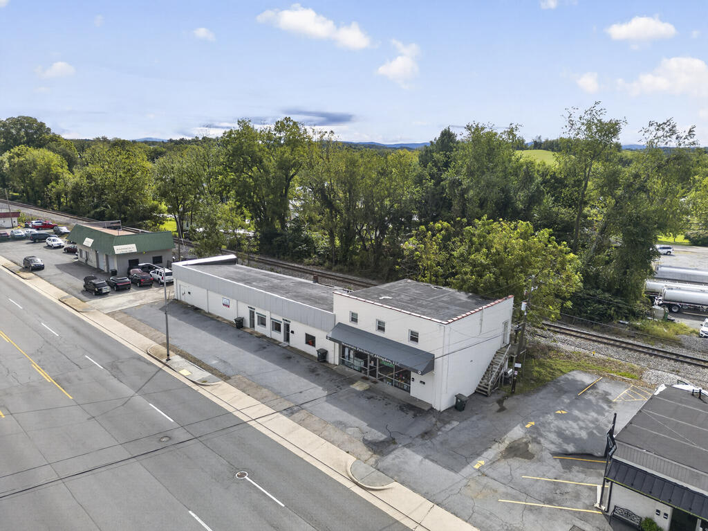 Aerial view of a white commercial building beside a main road, with parking and railroad tracks nearby.