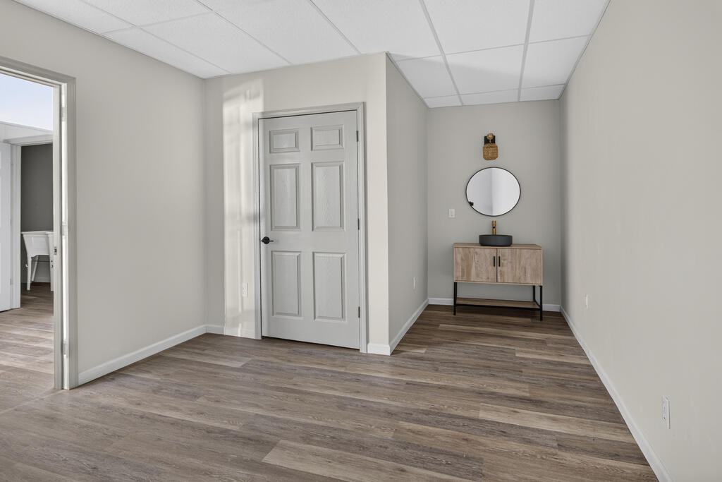 Vacant room with wood-look floors, a white paneled door, and a vanity beneath a round mirror.