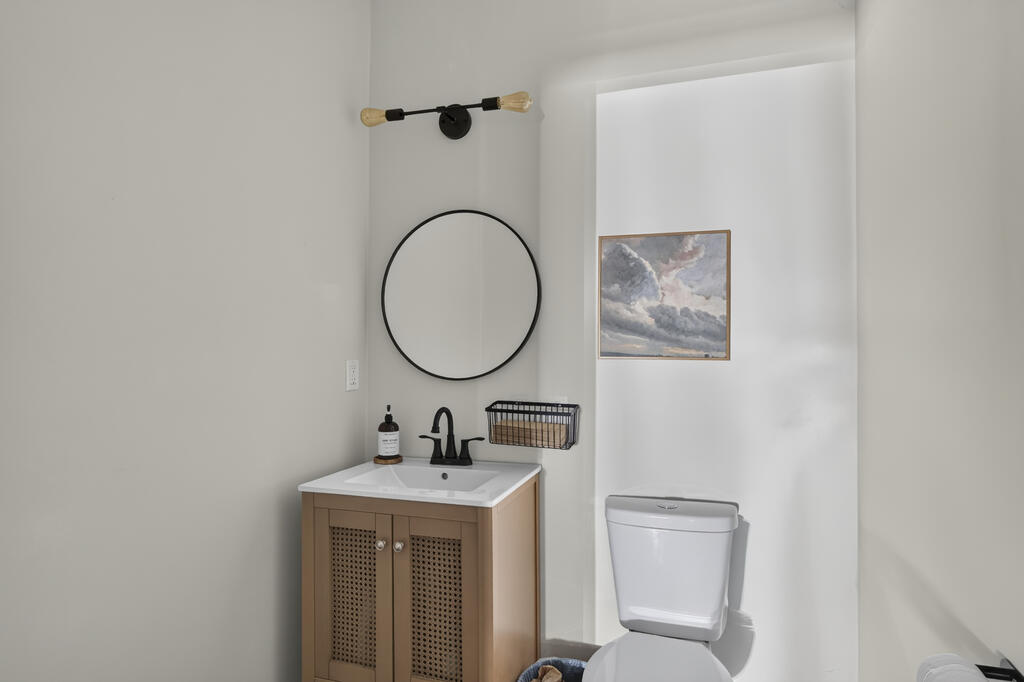 Bathroom with a cane-front vanity, round mirror, black faucet, and framed cloud painting.