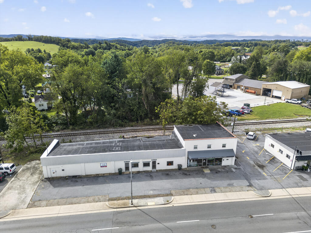 Low white commercial building beside the road, viewed from above with railroad tracks behind it.