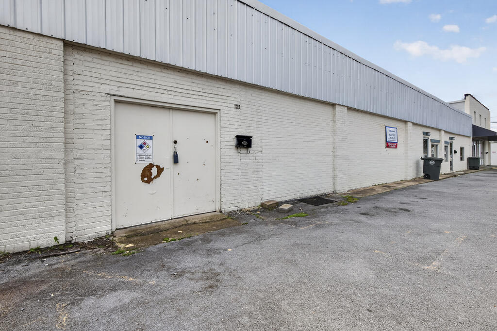 Commercial building exterior with white brick walls, a large service door, and paved parking area.