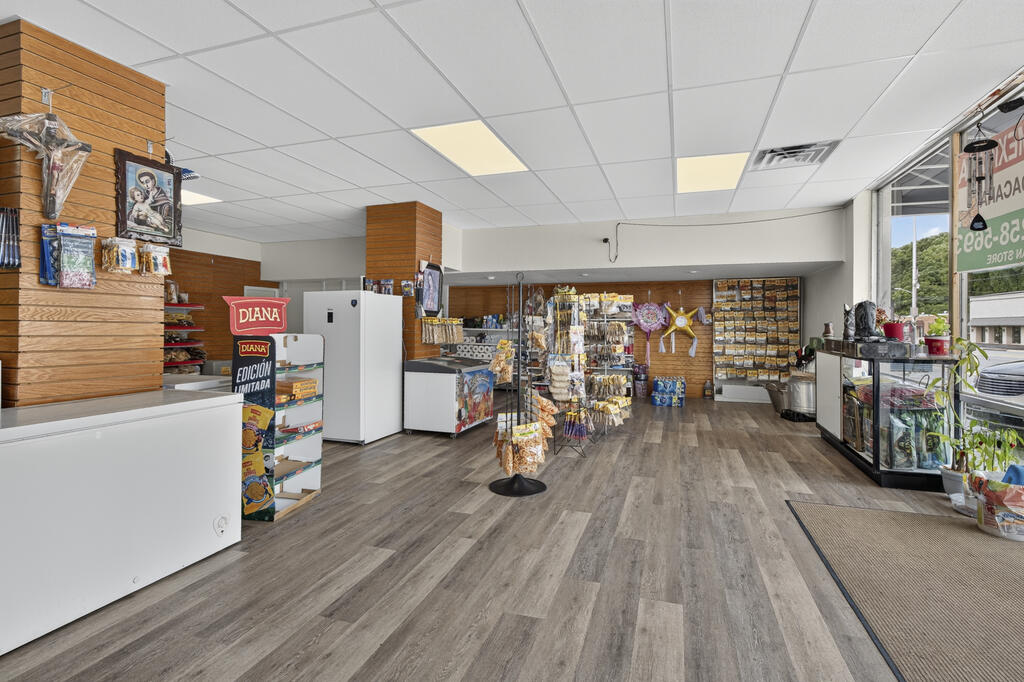 Convenience store interior with stocked shelves, a central snack rack, freezers, and glass-front coolers.