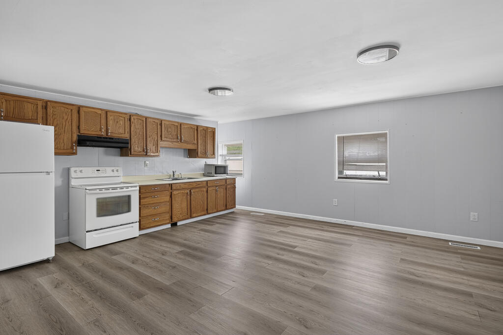 Unfurnished kitchen with wood cabinets, white appliances, and an open area with wood-look flooring.