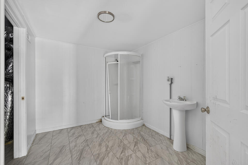 Bathroom with a curved glass shower, pedestal sink, and gray marble-look tile floor.