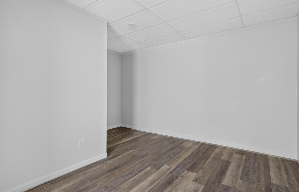 Vacant room with white walls, a suspended tile ceiling, and dark plank flooring.