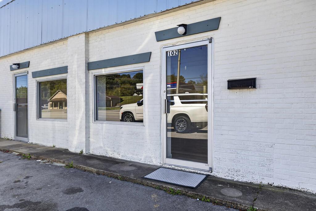 White brick commercial storefront with dark awnings, large windows, and glass entrance marked 102.