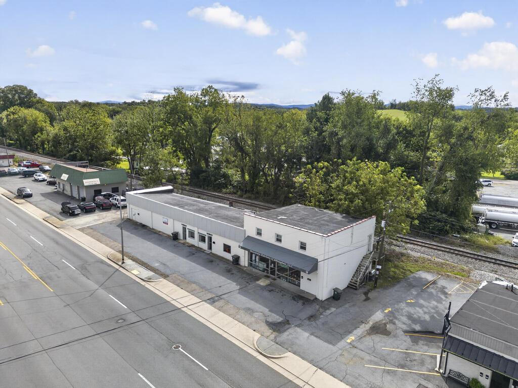 Aerial view of a long white commercial building beside Main Street, with railroad tracks and wooded hills behind it.