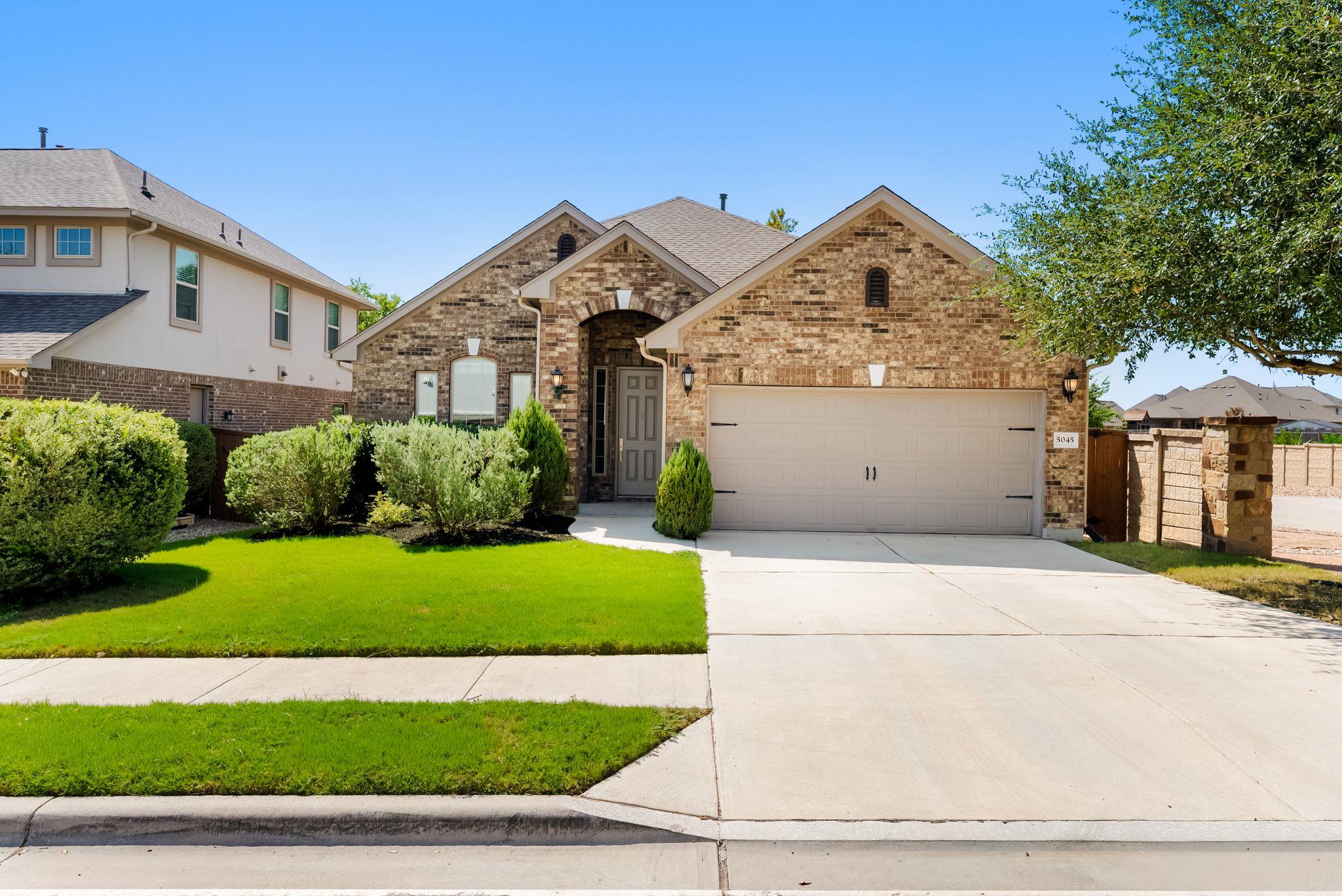 Brick house with double garage, trimmed shrubs, green lawn, and wide driveway.