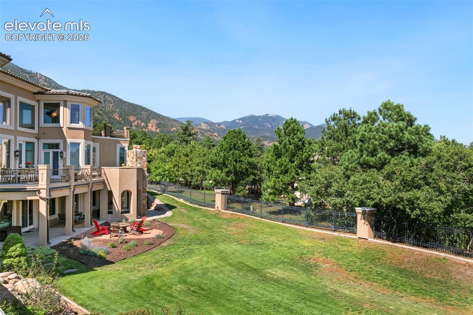 Home’s rear patio and fenced lawn with mountain views beyond the trees.