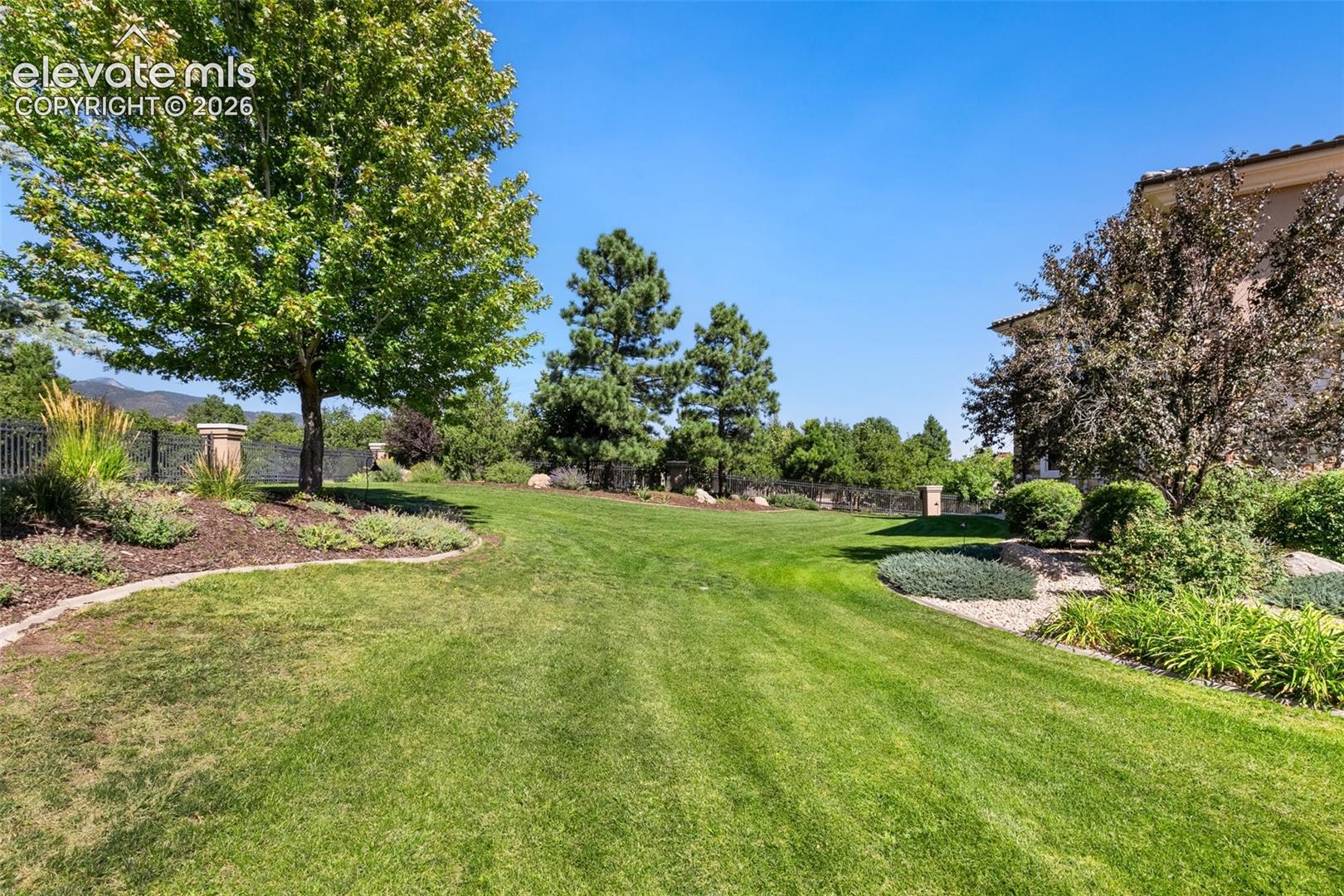 Landscaped lawn with mature trees, garden beds, and distant mountain views beside the home.