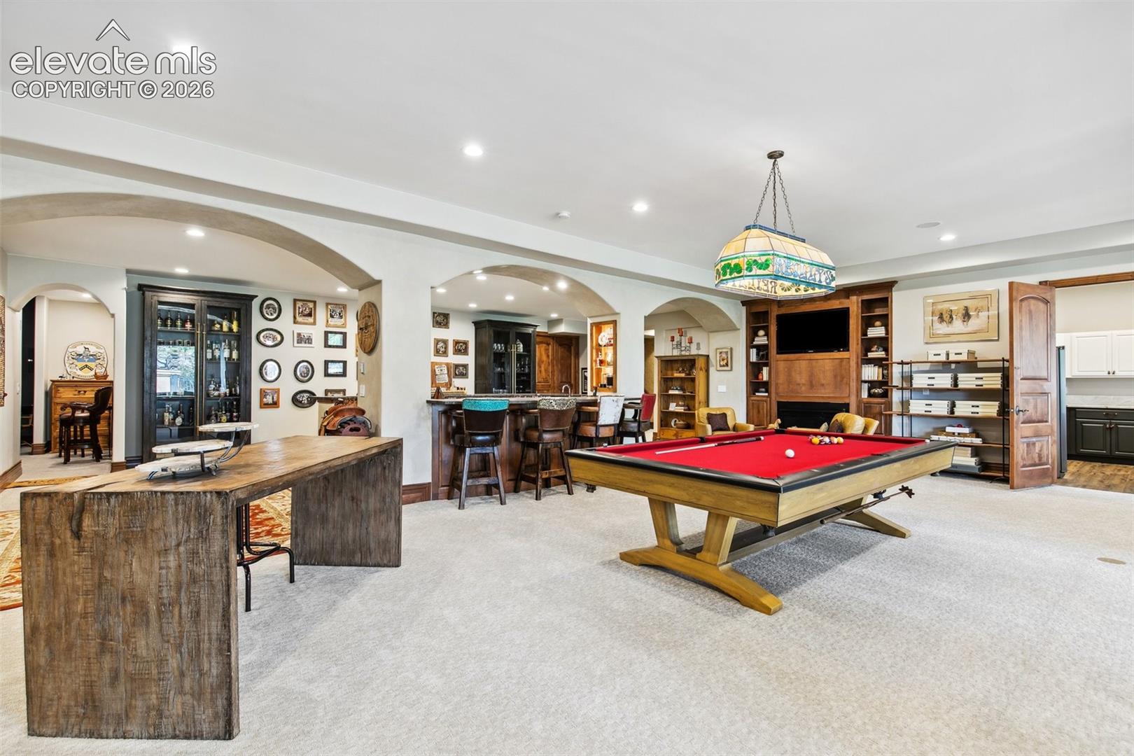 Recreation room with a red-felt pool table, wood bar, built-in shelving, and arched openings.