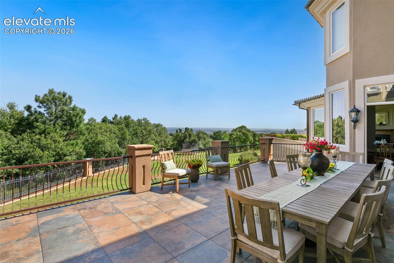 Tiled outdoor terrace with a wooden dining set, decorative railing, and views over trees and distant landscape.