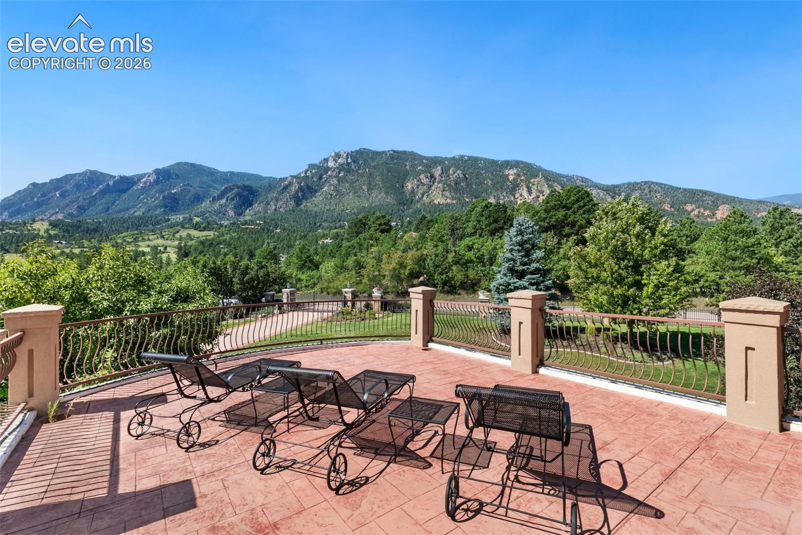 Terrace with black metal lounge chairs overlooking a green valley and forested Rocky Mountain peaks.