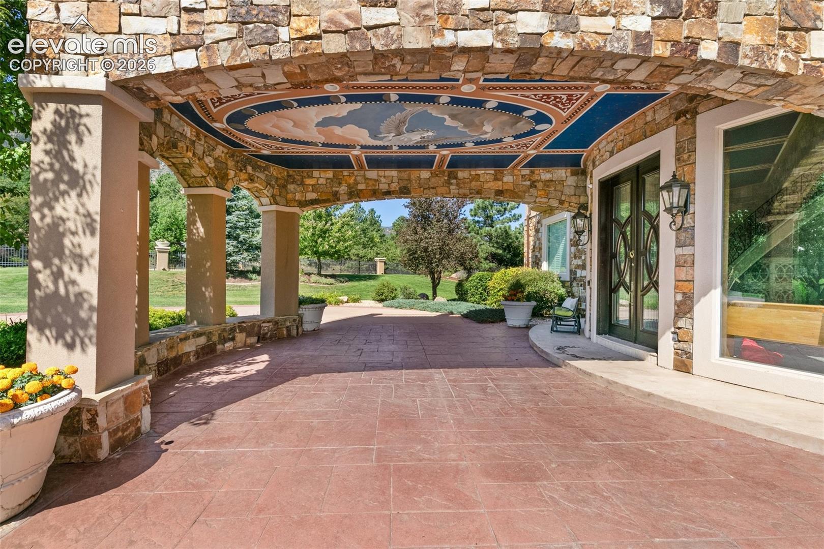 Stone-arched covered entry with a painted ceiling, dark double doors, and landscaped grounds.