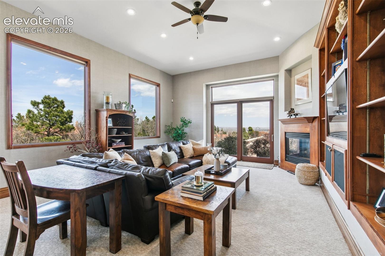 Living room with a leather sectional, built-in shelving, fireplace, and large windows.