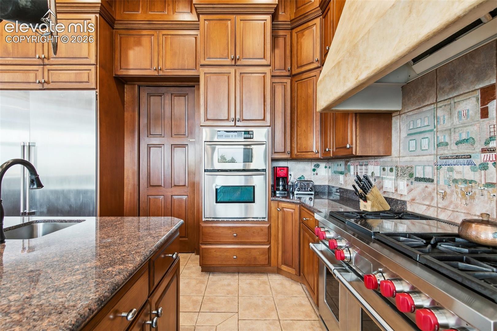 Kitchen with extensive wood cabinetry, granite counters, stainless appliances, and an illustrated tile backsplash.