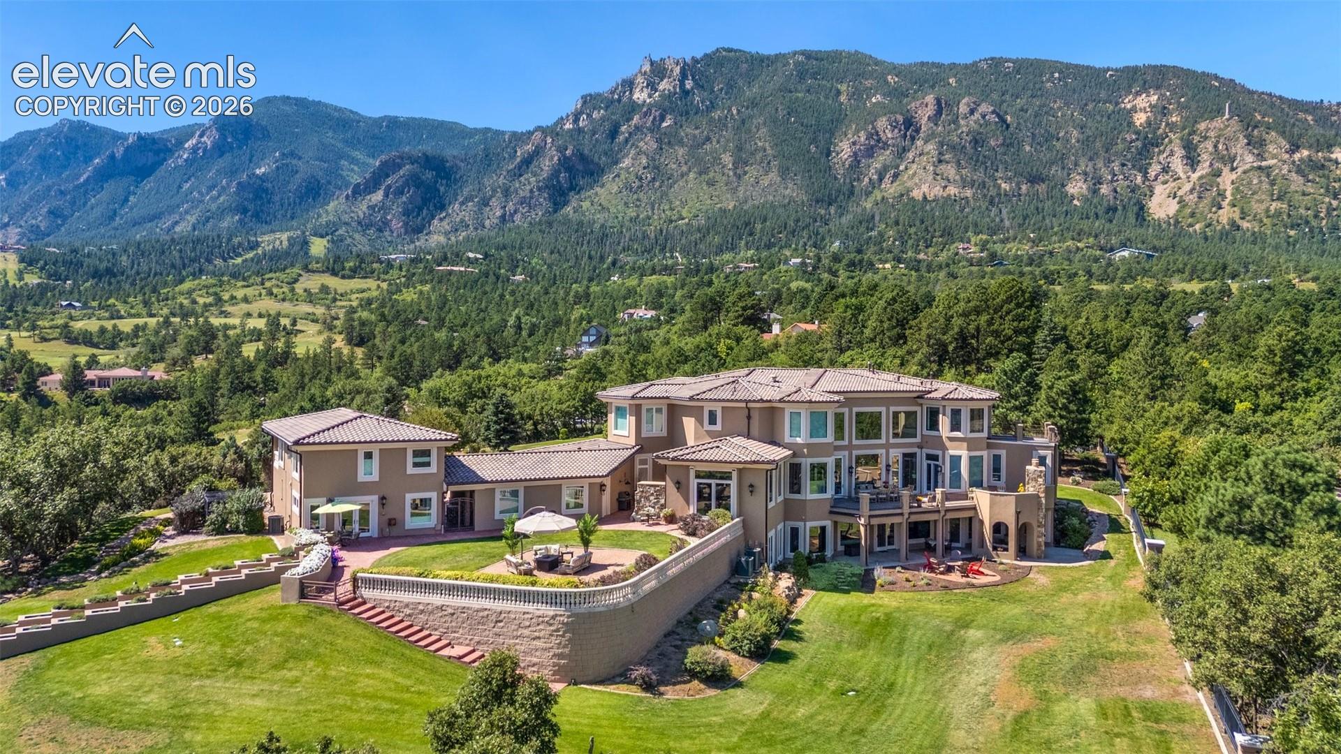 Aerial view of a large home with terraced lawns and forested mountains behind it.