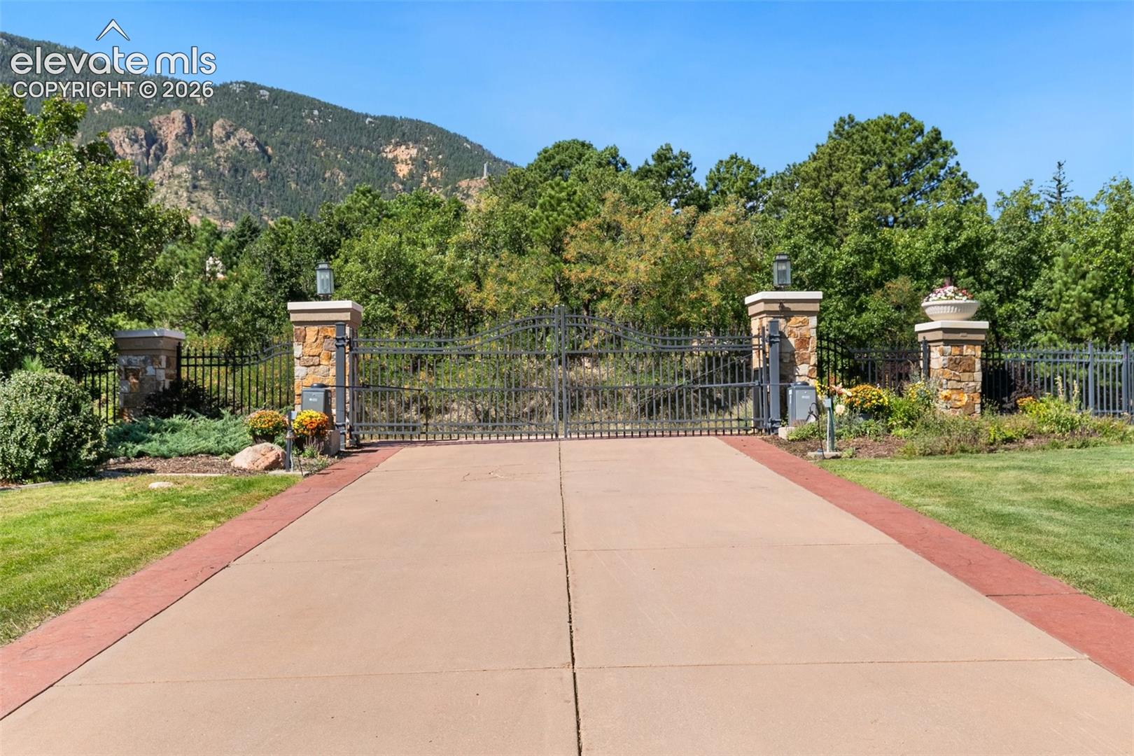 Gated property entrance with stone pillars, iron fencing, and a mountain backdrop.