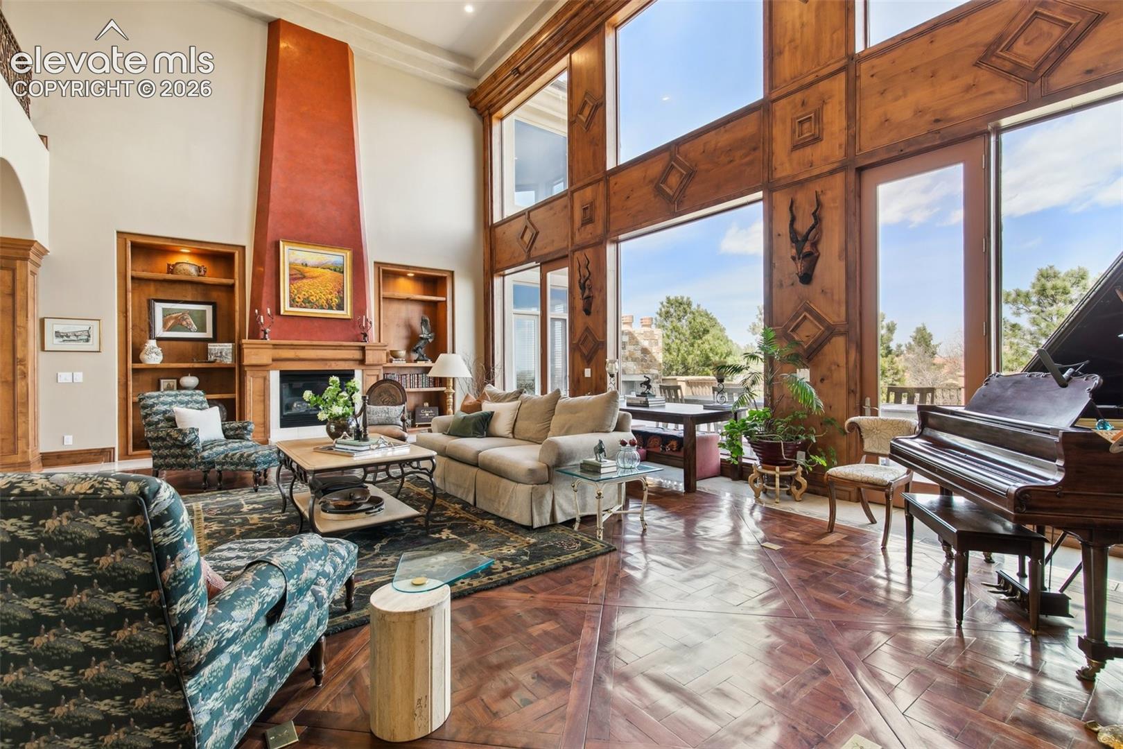 Living room with soaring windows, a wood-paneled wall, fireplace, and grand piano.