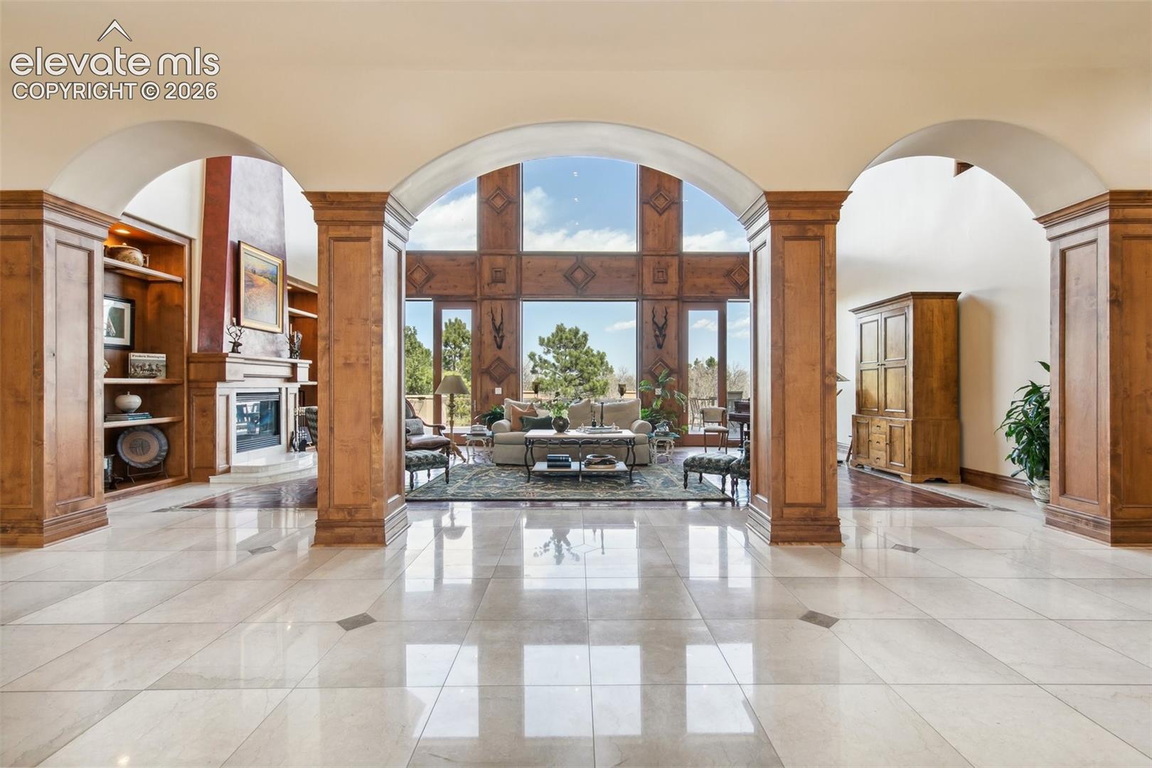Grand tiled entry with three arches opening to a wood-paneled living room and fireplace.
