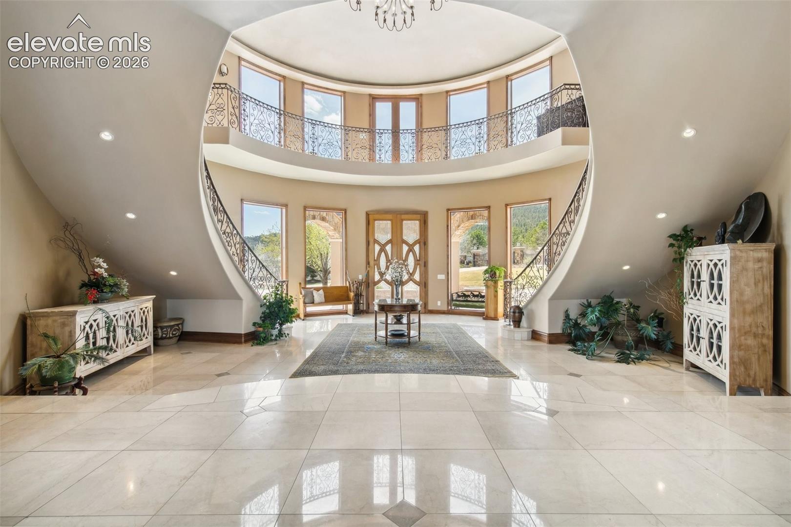 Two-story foyer with a curved iron-railed balcony, tall windows, and polished tile floors.