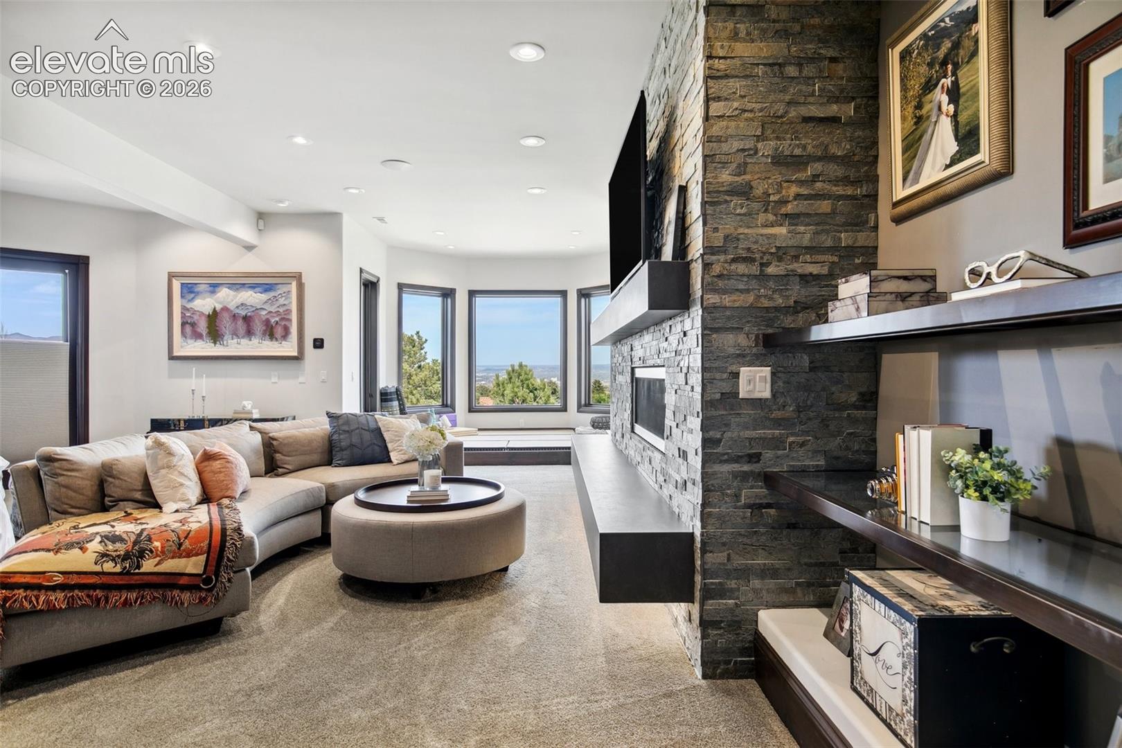 Living room with a gray sectional, stacked-stone fireplace wall, and large windows.