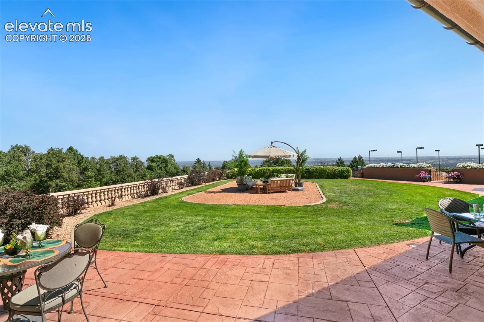 Backyard patio and lawn with umbrella-shaded seating and a distant landscape view.