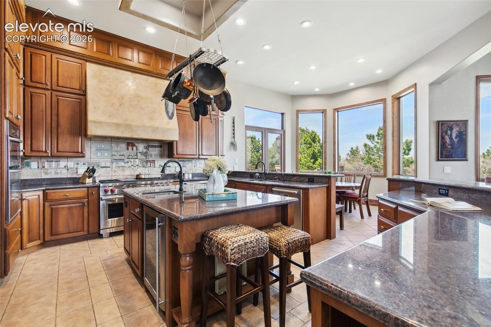 Spacious kitchen with wood cabinetry, granite counters, a large island, and tall windows overlooking trees.