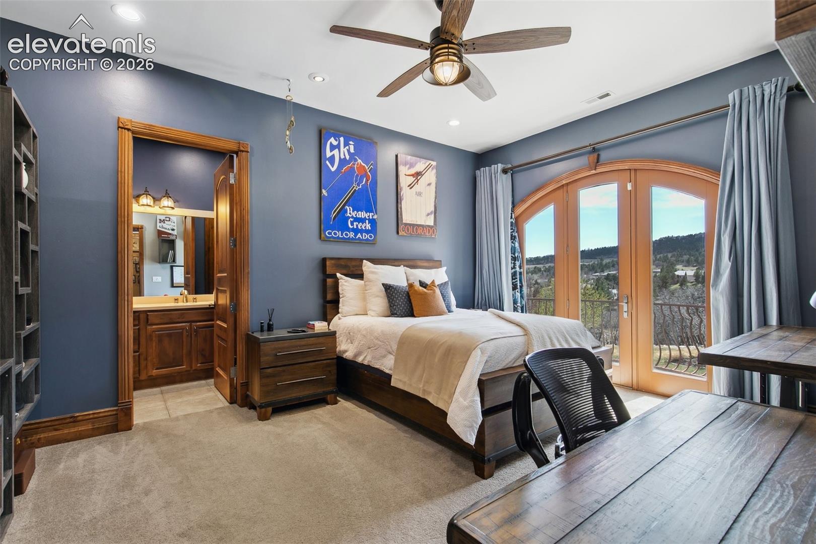 Furnished bedroom with blue walls, arched balcony doors, and foothill views.