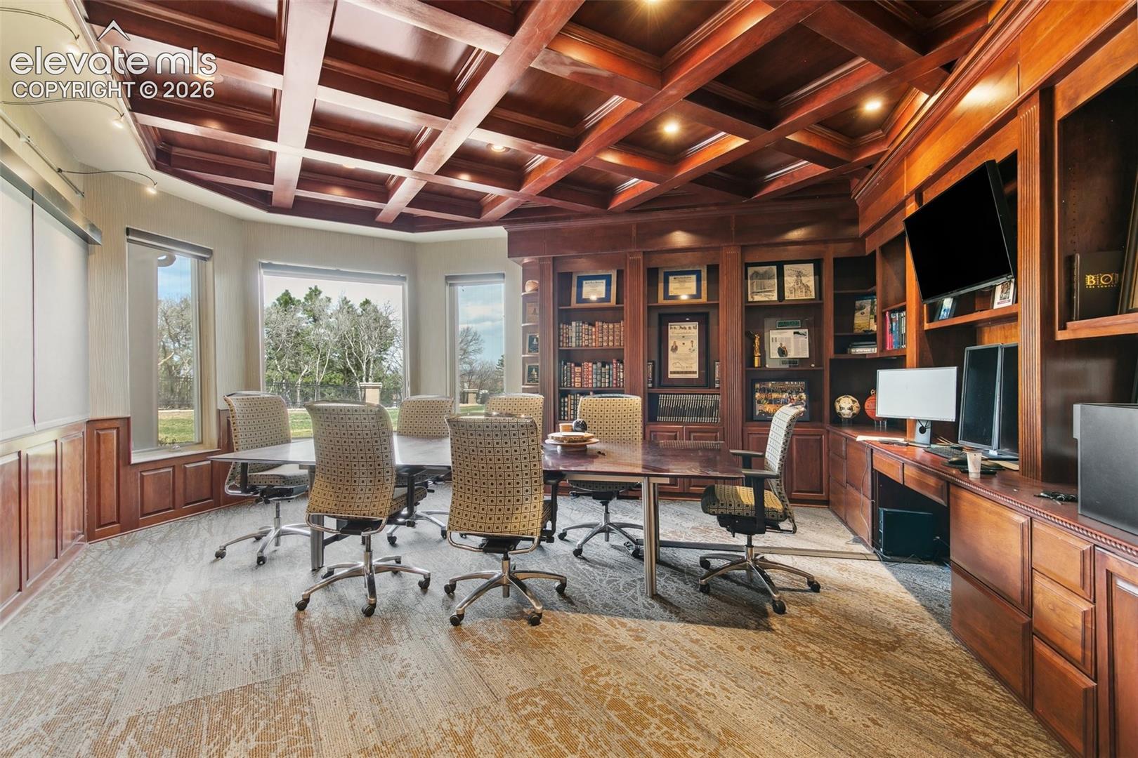 Furnished home office with conference table, built-in bookcases, and a coffered wood ceiling.