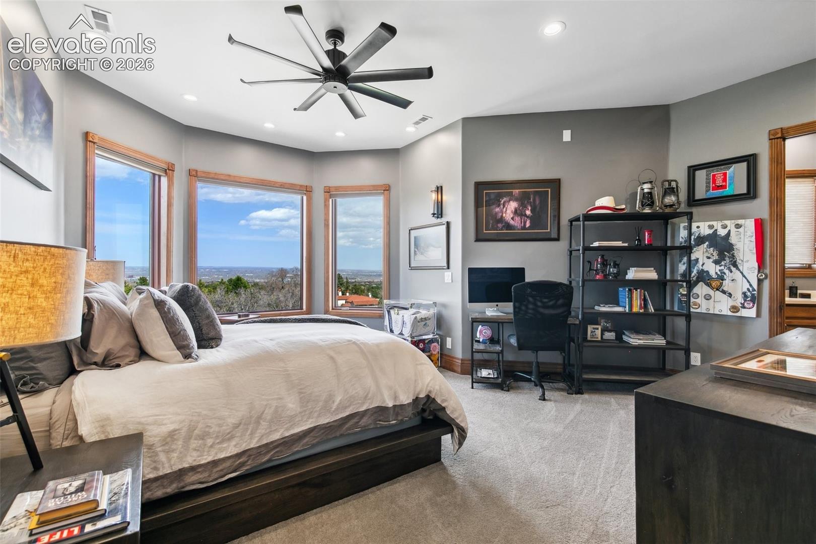 Furnished bedroom with a large bed, three wood-trimmed windows, and distant city views.