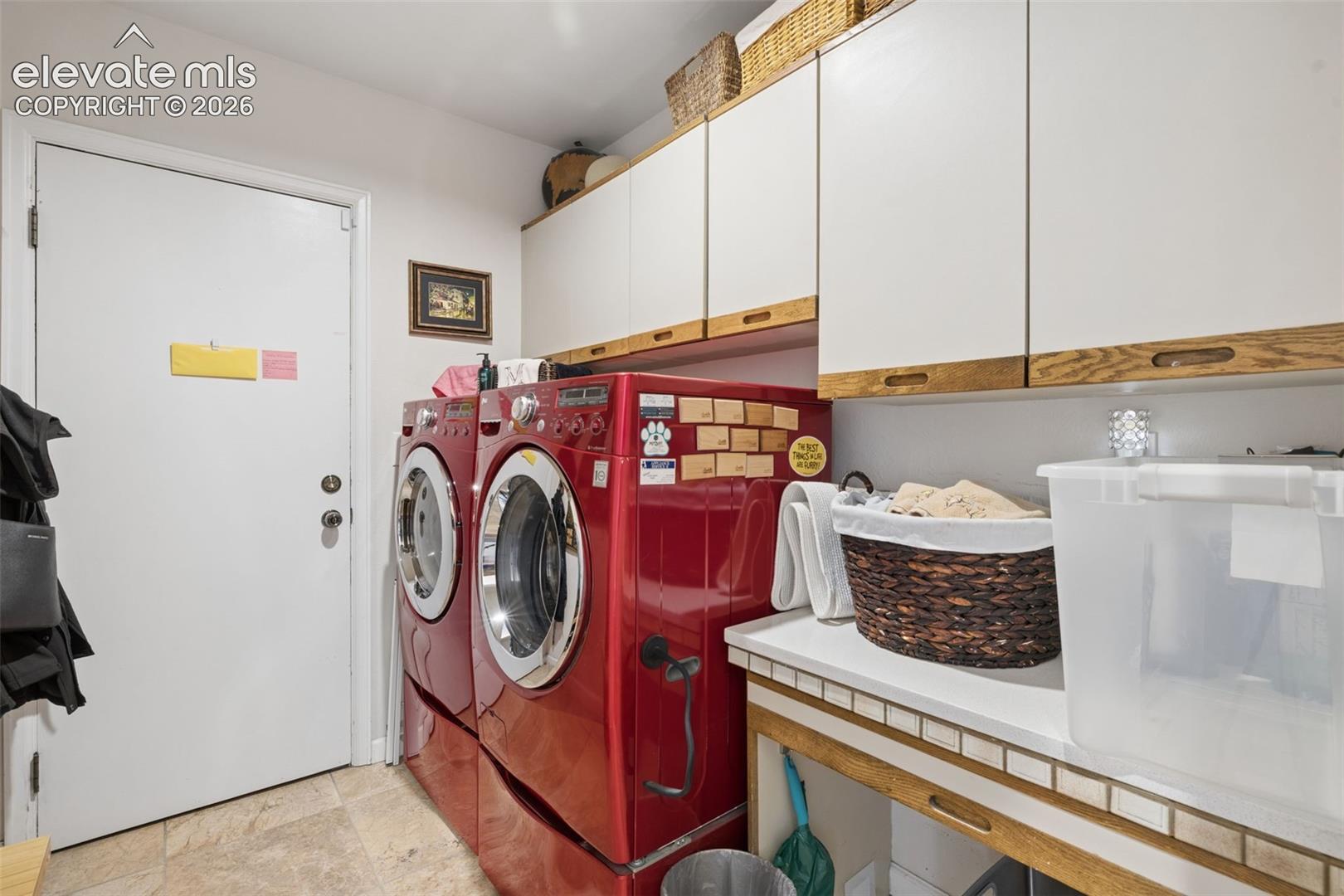 Laundry room with red front-loading washer and dryer, white cabinets, and a tiled utility counter.